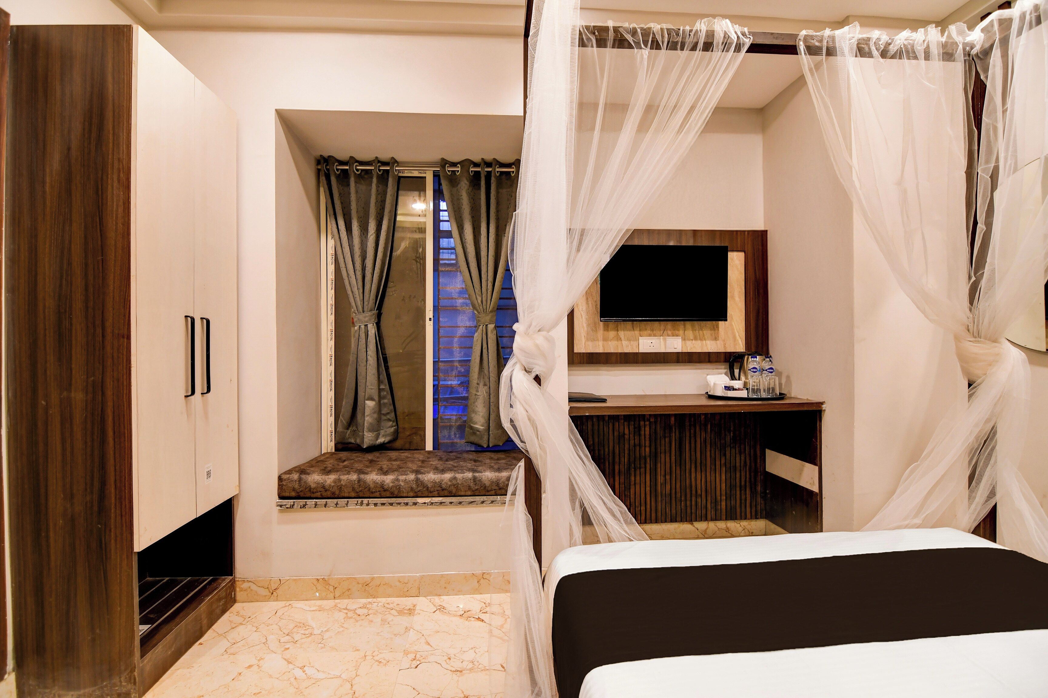 A hotel room with a bed, a TV, a small window with curtains, and a vanity area.