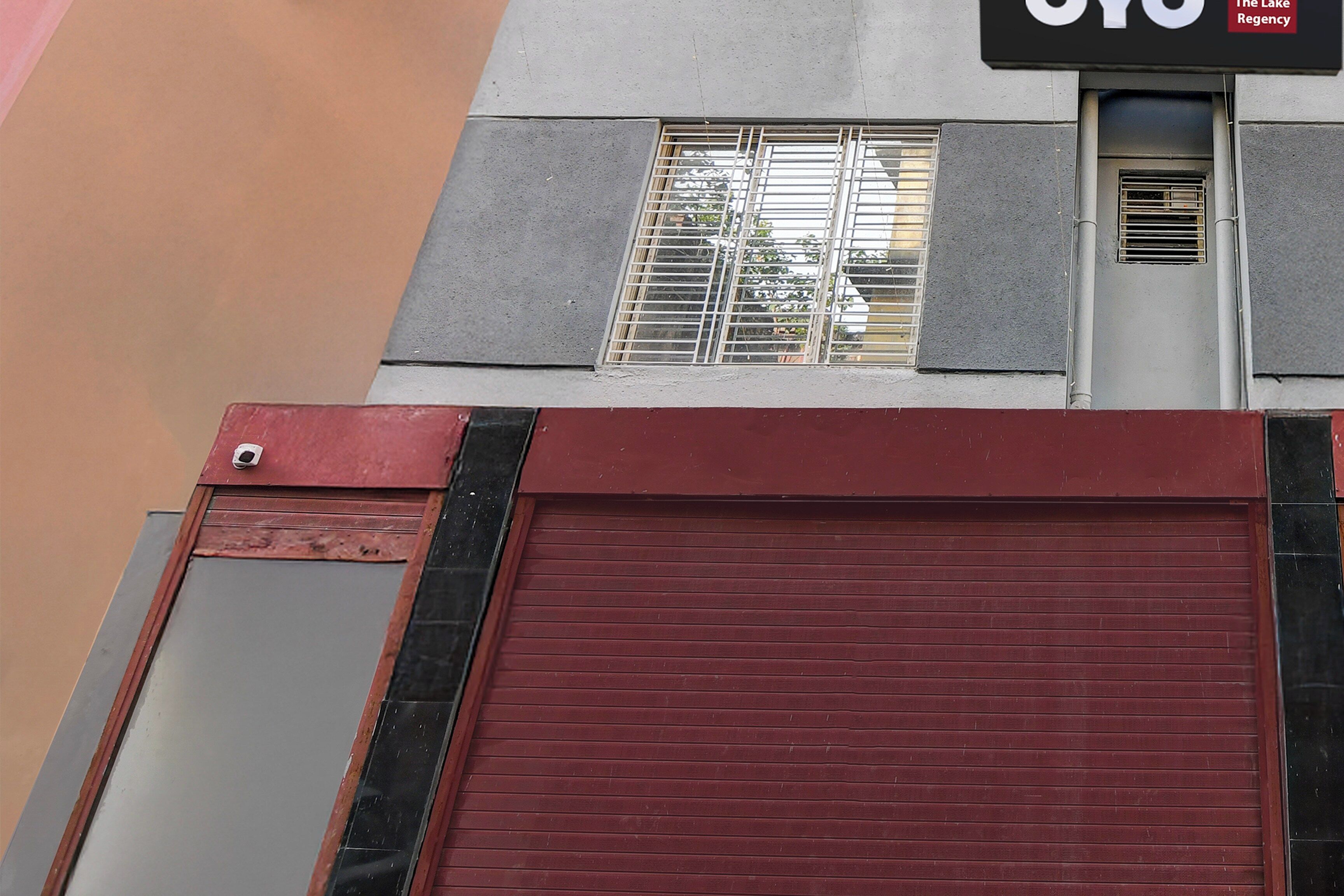 A building facade with a red shuttered garage door, a window with metal bars, and a sign above the window.