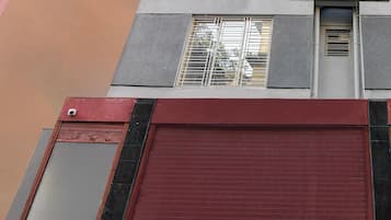 A building facade with a red shuttered garage door, a window with metal bars, and a sign above the window.