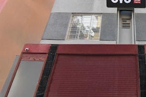 Fachada de edificio con puerta de garaje con contraventanas rojas, una ventana con rejas y un letrero sobre la ventana.