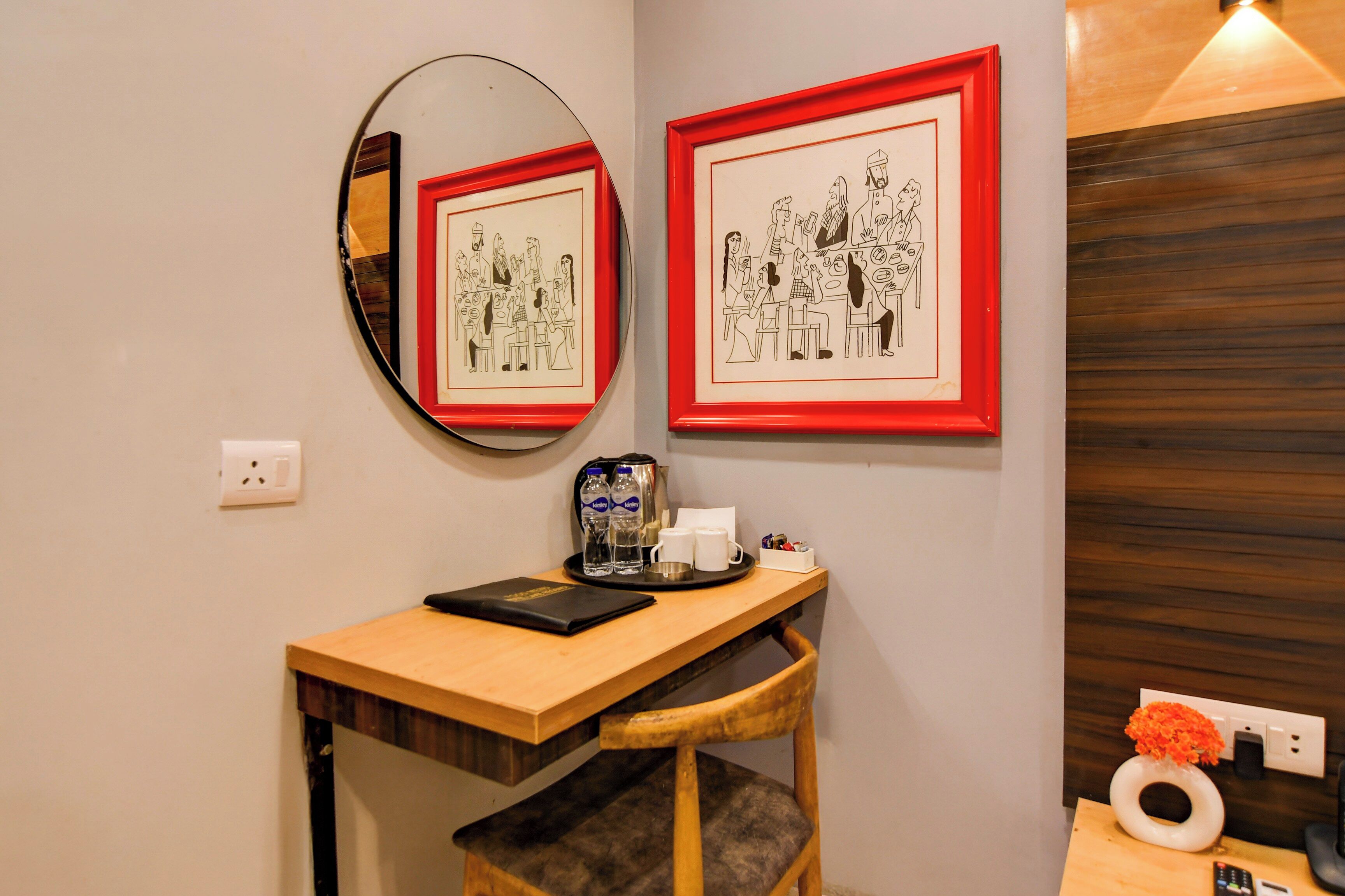 A room with a wooden desk, a chair, a mirror, and two framed black-and-white illustrations on the wall.