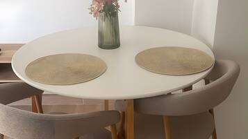 Una mesa de comedor redonda con dos individuales tejidos, un florero con flores y un par de sillas tapizadas.
