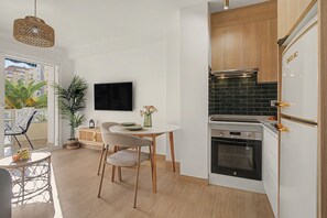 A modern kitchen with a built-in oven, a dining area with a round table and chairs, and a view of the outside balcony.