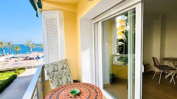 A balcony with a table and chairs, a view of the sea, and a glass door leading to an interior space.