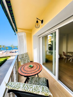 Un balcone con tavolo e sedie, vista sul mare e una porta vetrata che dà su un ambiente interno.