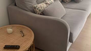 Un salón moderno con un sofá gris, cojines estampados, una mesita redonda de mimbre y una lámpara de pie.