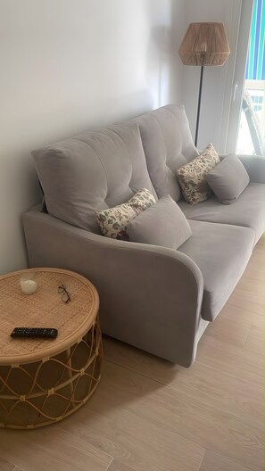 Un soggiorno moderno con un divano grigio, cuscini decorati, un tavolino rotondo in vimini e una lampada da terra.