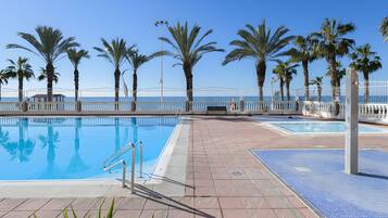 Una piscina con un borde de baldosas, palmeras y vista al mar.