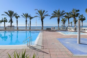 Una piscina con bordo piastrellato, palme e vista sul mare.