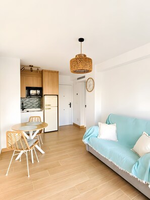 Un espai modern d'estar amb cuina, zona de menjador i un sofà blau clar.