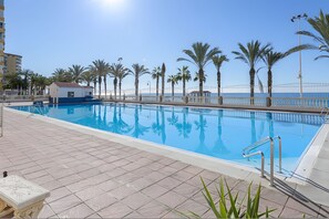 Piscina amb terrassa enrajolada, envoltada d'arbres de palmera i una tanca blanca.