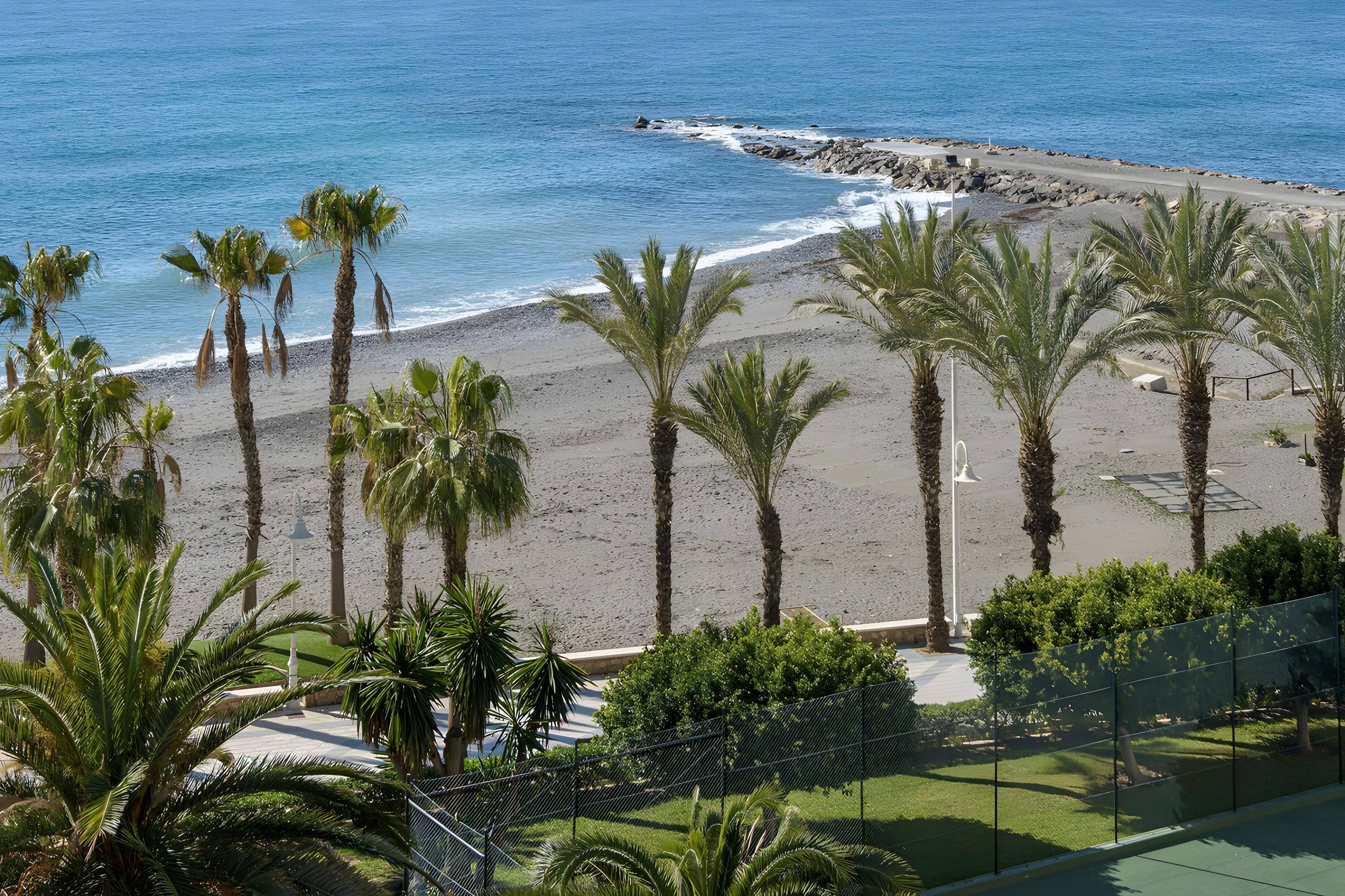 Una playa con palmeras y un litoral rocoso.