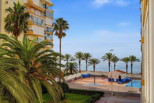 A beachfront property with a pool, palm trees, and a view of the sea.