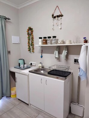 A compact kitchenette with a sink, a kettle, a coffee maker, and a small cabinet. - Room-charming Overnight Granny Flat With (Cape Town)