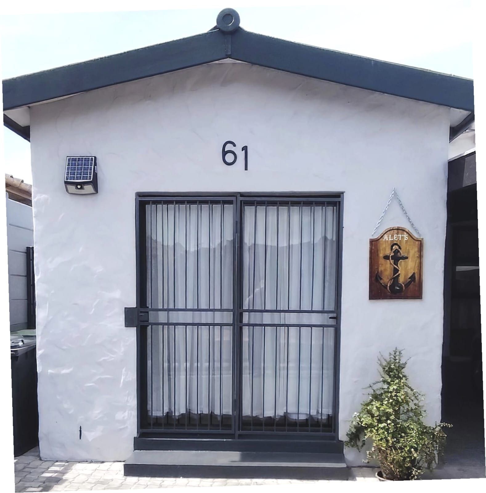 Un edificio con un ventanal grande de marco negro, un pequeño panel solar y un letrero de madera con la inscripción 'A LET'S' a la derecha.