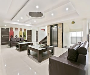 A modern living room with a sofa, coffee table, and a staircase leading to an elevator. - Deluxe Halcyon Deccan Inn (Hyderabad)