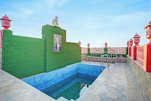 Una piscina con pared verde y un mural, rodeada por una cerca roja y rosa.