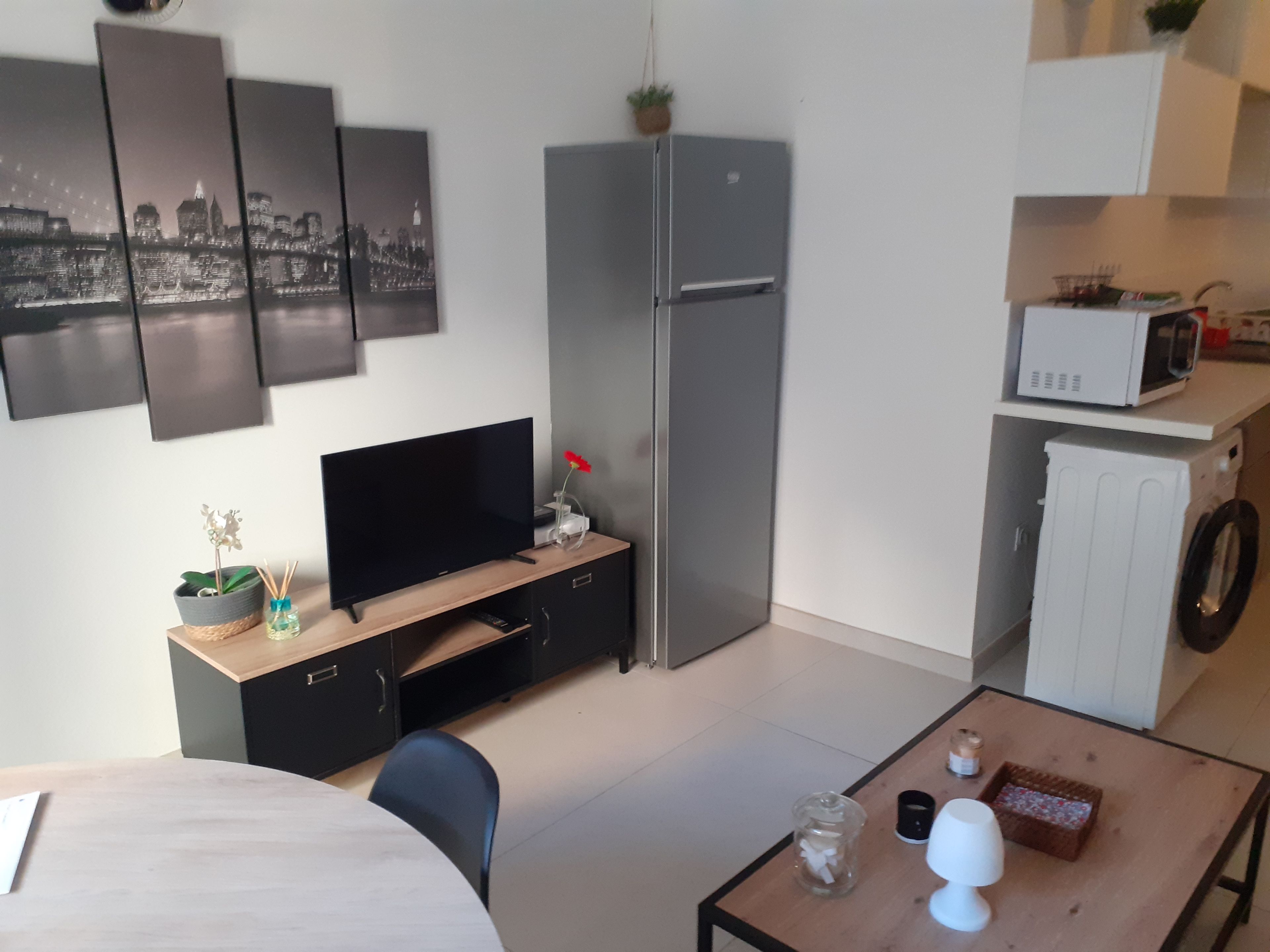 Un espacio habitable compacto con televisión de pantalla plana, refrigerador, microondas, lavadora y comedor con mesa y sillas.