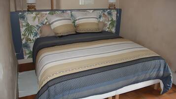 Uma cama com cabeceira estampada, duas luminárias de apoio e uma parede com um quadro emoldurado.