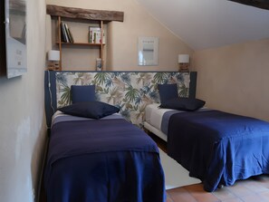 Quarto com duas camas, uma estante de madeira com livros, um espelho e um candeeiro fixado na parede.