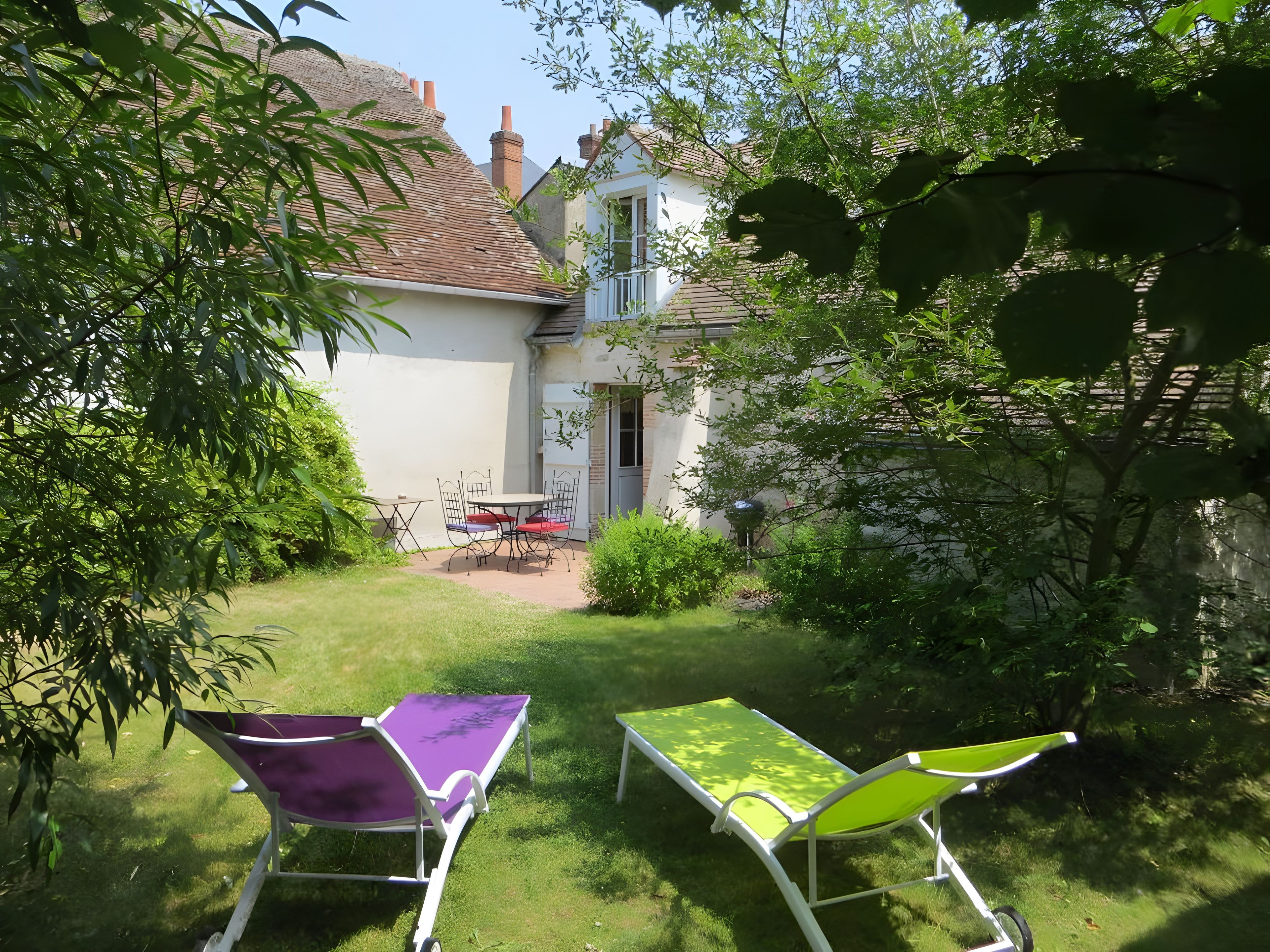 Een tuin met twee loungestoelen, een tafel en een gebouw op de achtergrond.