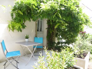 Área externa com mesa, duas cadeiras e vegetação, cercada por um muro branco.