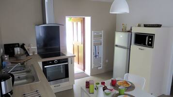 Een moderne keuken met een ingebouwde oven, magnetron en een groot fornuis. Er is een eethoek met een tafel voor twee personen, en een koelkast met een magnetron erboven.