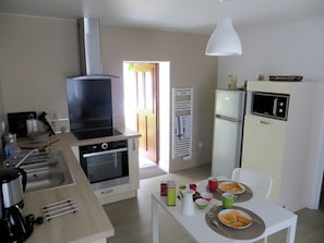 Cuina moderna amb forn integrat, microones i una fornet gegant. Hi ha una zona de menjador amb una taula preparada per a dues persones, i un frigorífic amb un microones a sobre.
