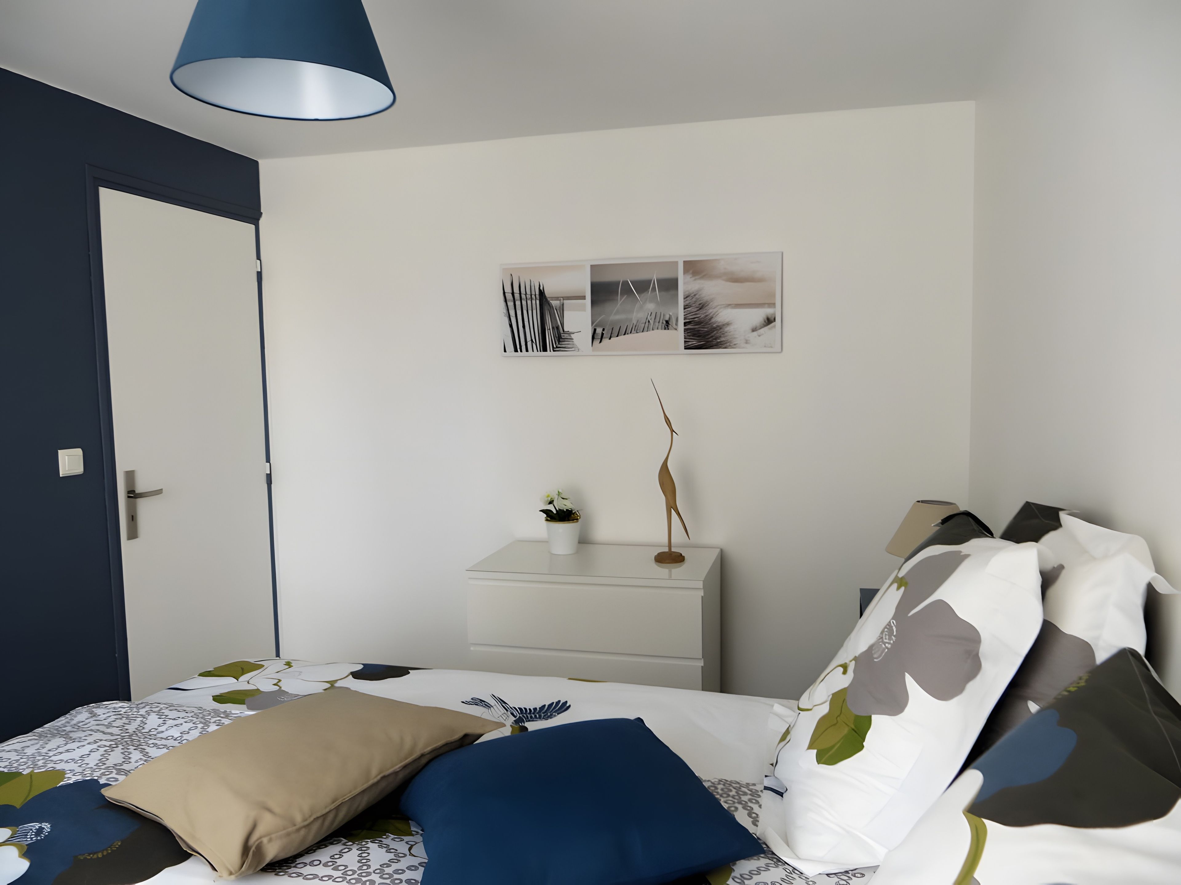 Et soveværelse med seng, et natbord med lampe, en dør og billedkunst på væggen.