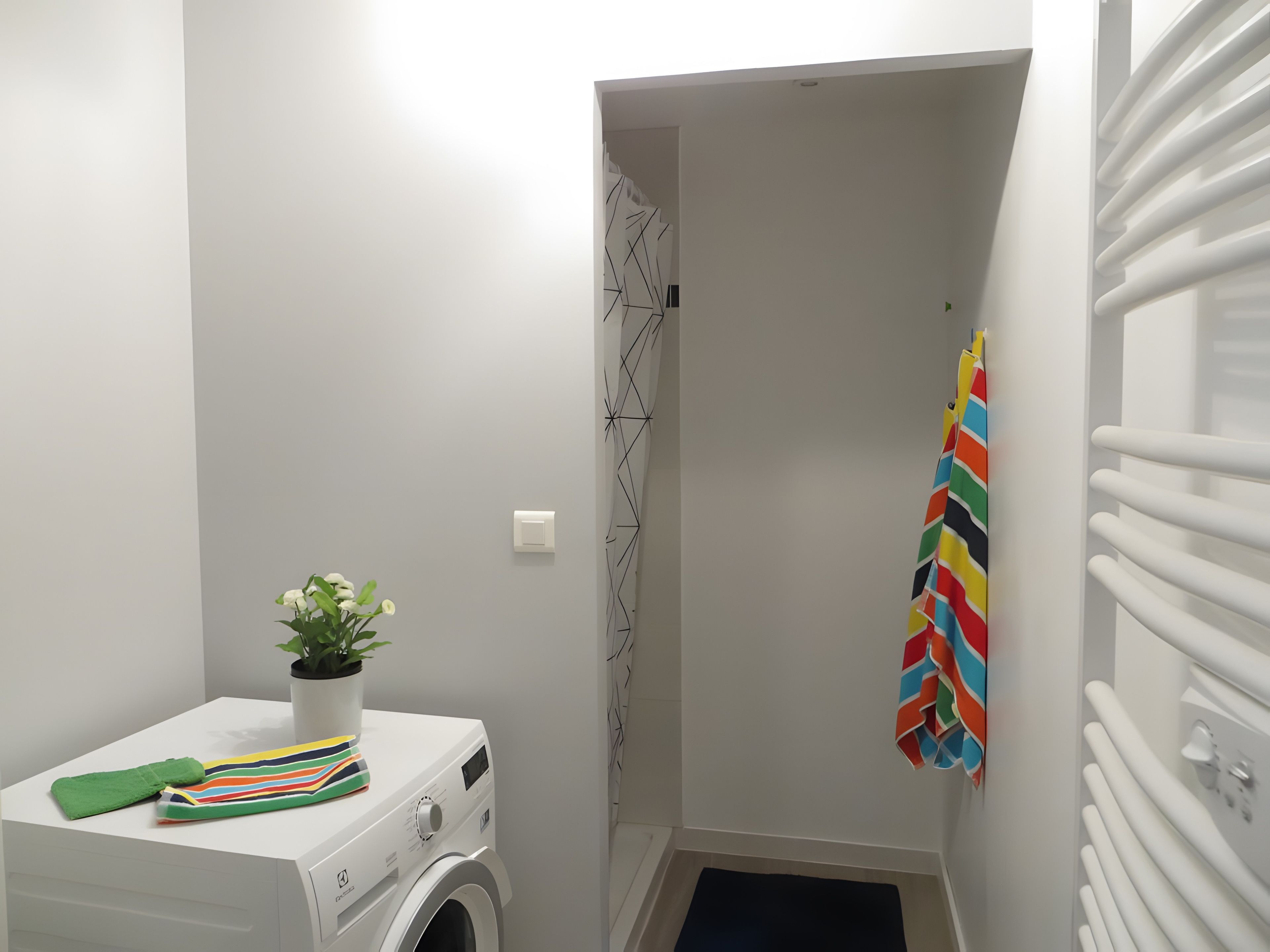 Een kleine wasruimte met een wasmachine, een droogrek en een kleine plant in een pot.