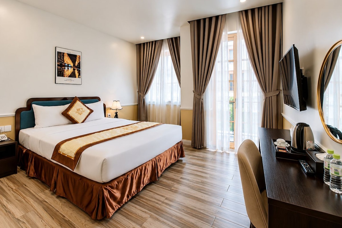 A hotel room with a large bed, a desk with a mirror, a TV, and a window with curtains.