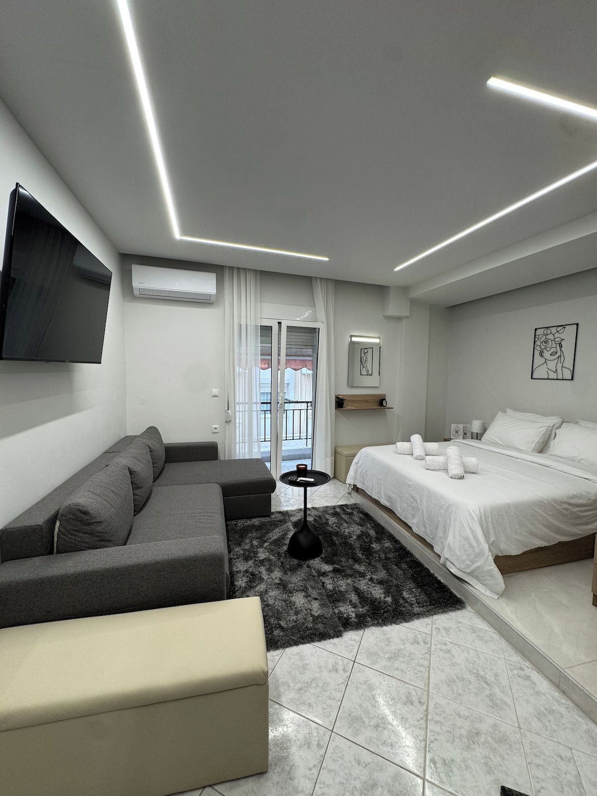 Una habitación de hotel moderna con sofá, cama, una mesita y televisor montado en la pared.