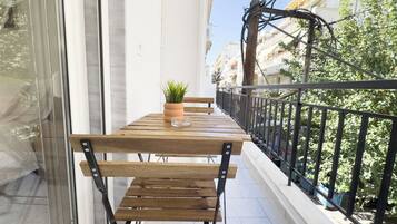 A balcony with a wooden table and benches, a potted plant, and a view of buildings and trees.