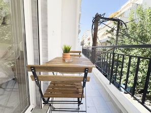 A balcony with a wooden table and benches, a potted plant, and a view of buildings and trees. - Velórea Exclusive Residences - Ándrea studio (Thessaloniki)