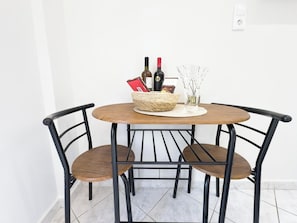 A round table with a woven basket containing bottles and a card, flanked by two chairs with metal frames and wooden seats. - Velórea Exclusive Residences - Ándrea studio (Thessaloniki)