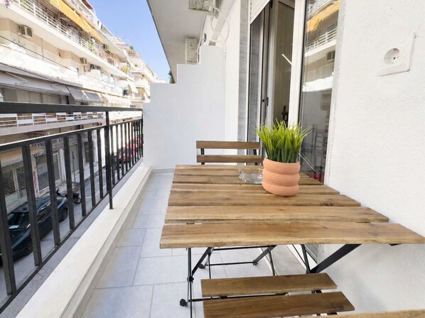 A wooden table with benches on a balcony, a potted plant, and a view of a cruise ship in the background. - Velórea Exclusive Residences - Ándrea studio (Thessaloniki)
