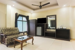 A living room with a sofa, a coffee table, a television, a refrigerator, and a ceiling fan. - Townhouse Jabalpur Railway Junction (Jabalpur)