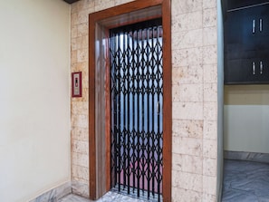A door with a metal security gate, a wall-mounted elevator control panel, and a tiled floor. - Townhouse Jabalpur Railway Junction (Jabalpur)