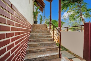 Una escalera con un muro de ladrillo a un lado y una barandilla al otro, que conduce a una zona cubierta con plantas en macetas.