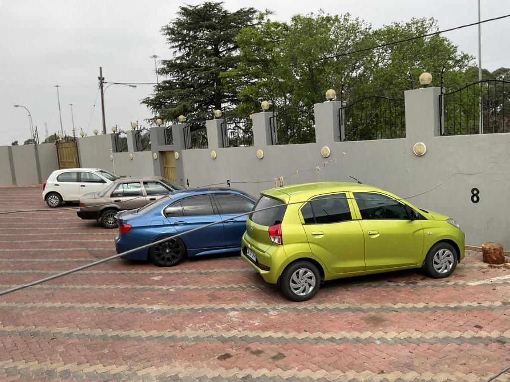 Un estacionamiento con coches aparcados en filas, una entrada con puerta de acceso y un muro con secciones numeradas.