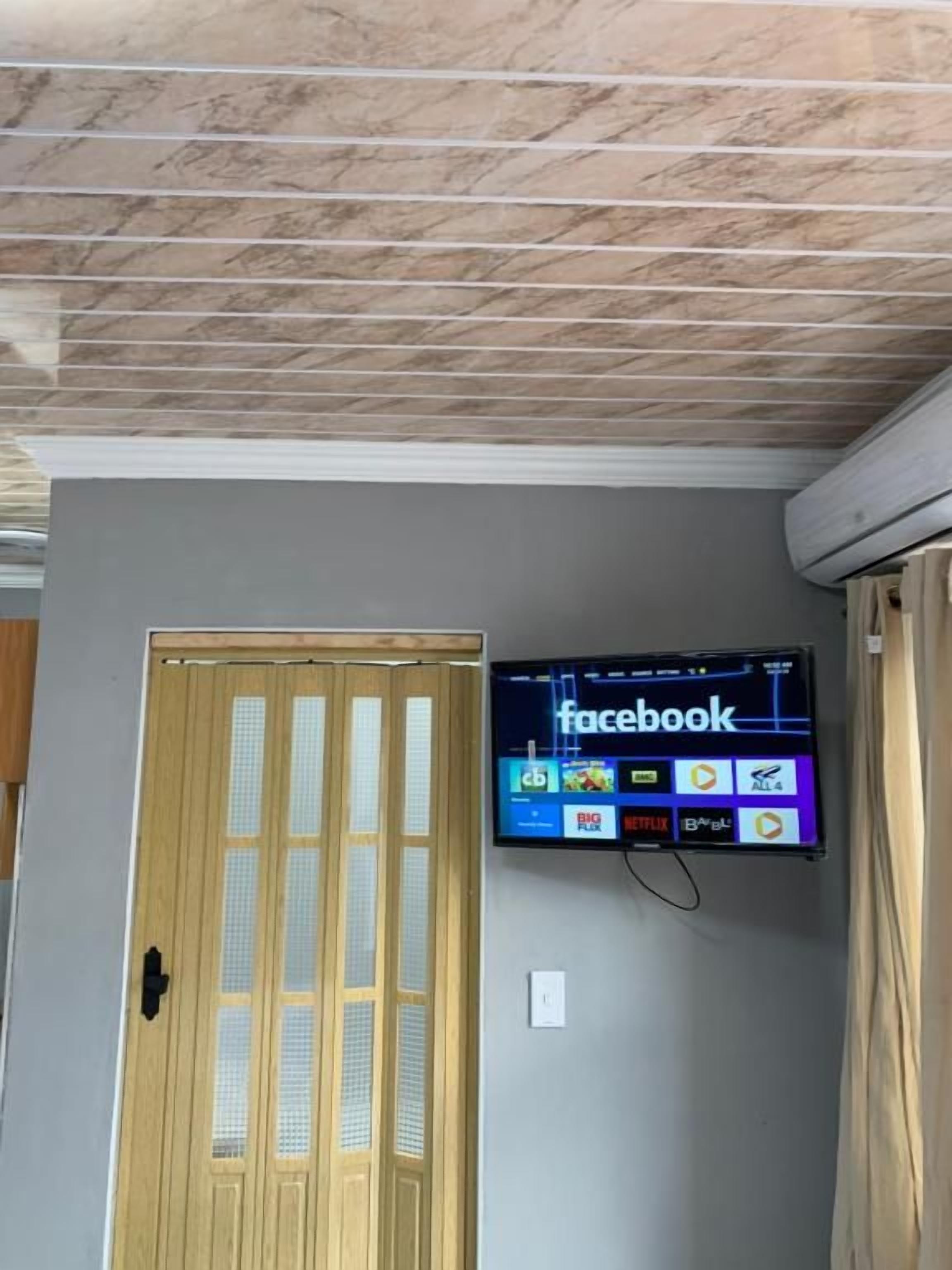 A room with a wooden door, a mounted television displaying the Facebook app, and a ceiling with a marble-like pattern.