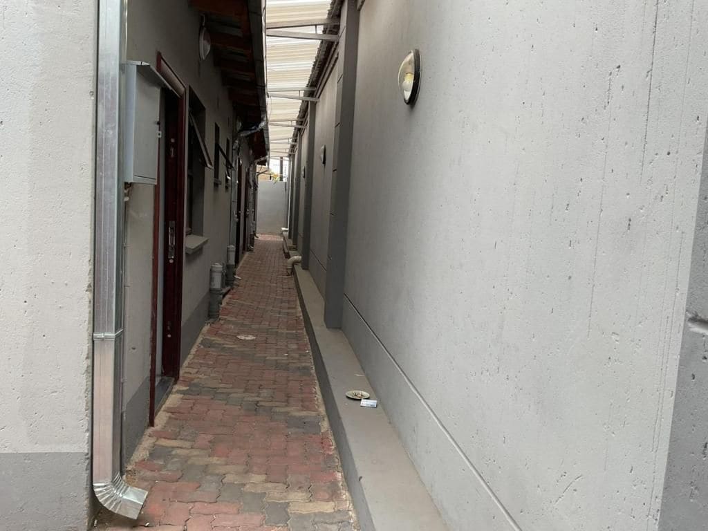 Un estrecho pasillo con piso de ladrillo, barandas de metal y una pared gris.