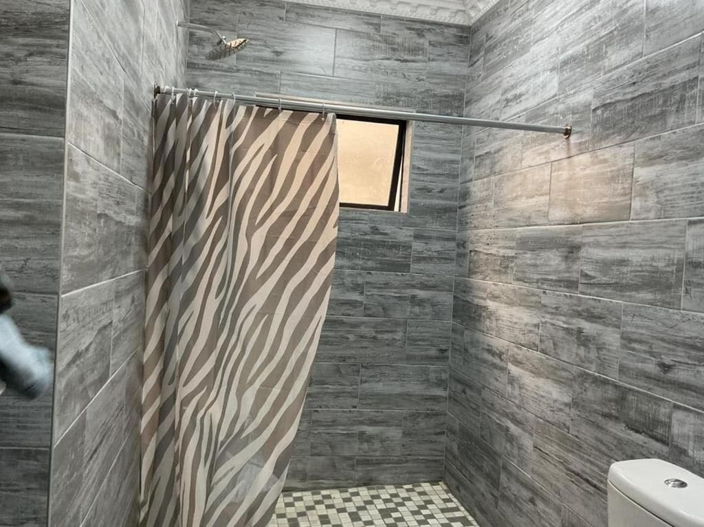 A bathroom with a shower area, a toilet, and a window.