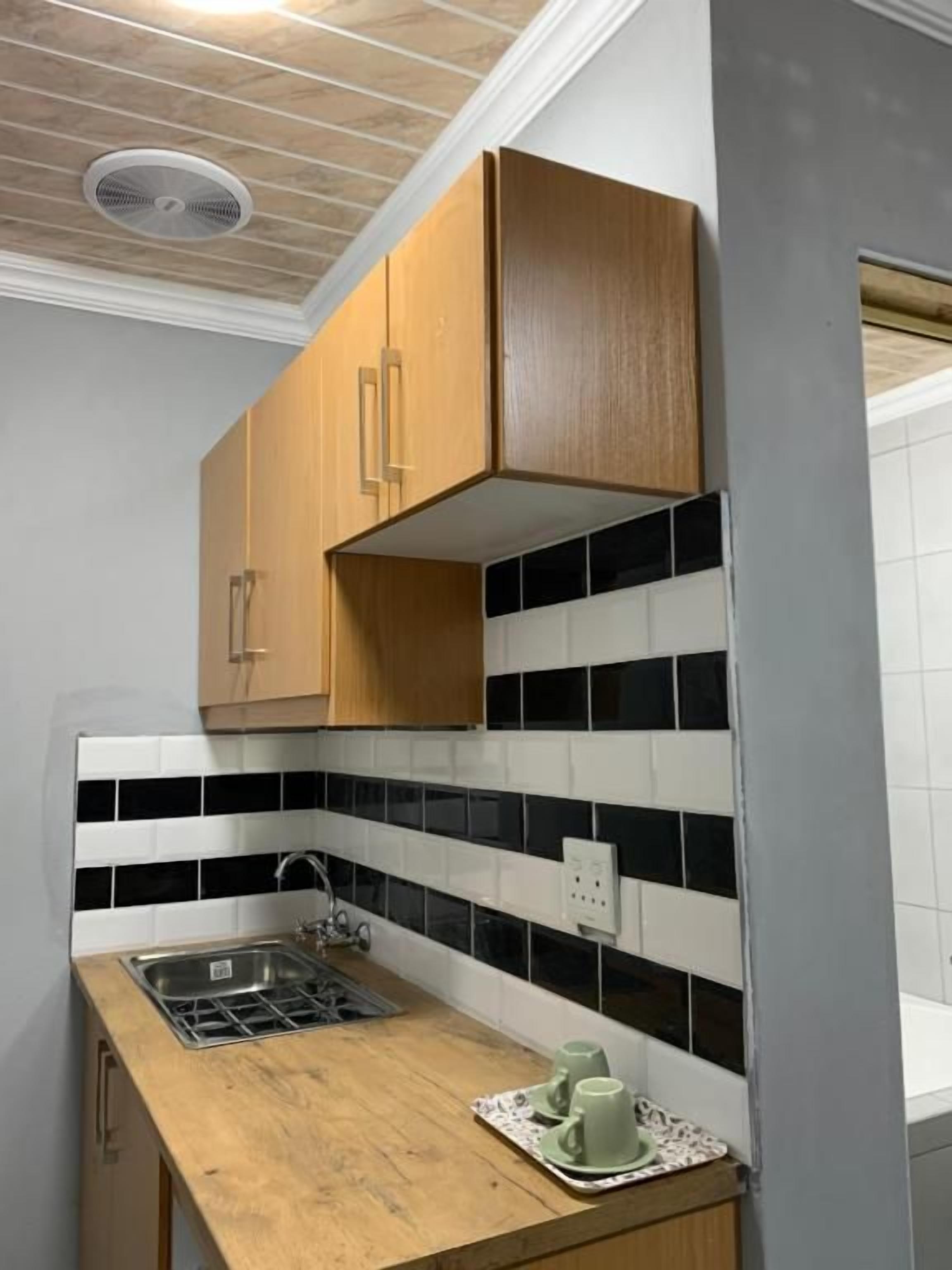 Cocina con armarios de madera, salpicadero blanco y negro y fregadero de acero inoxidable, además de encimera de madera.