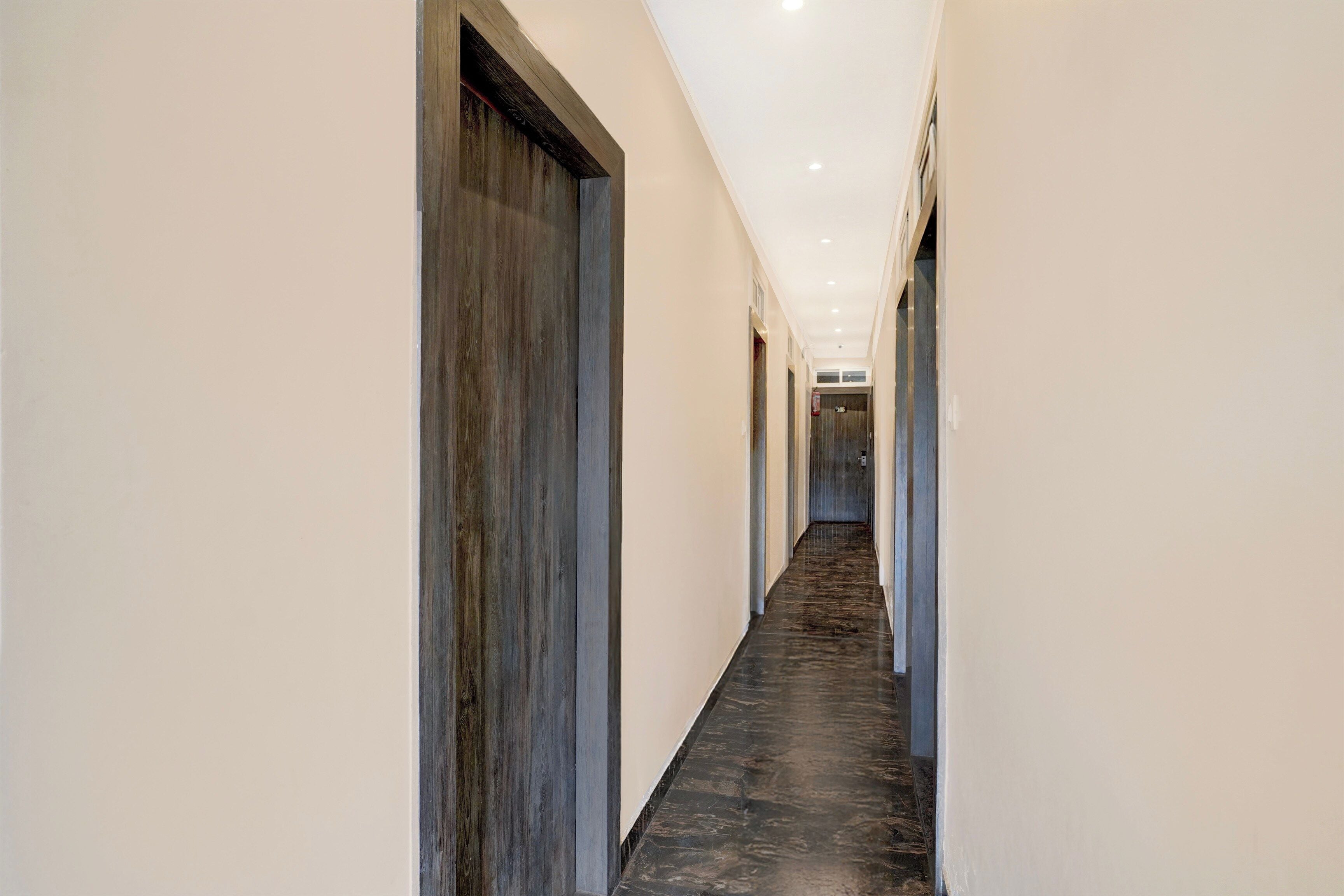 Un pasillo largo y estrecho con piso oscuro y paredes claras, que conduce a una puerta al final.