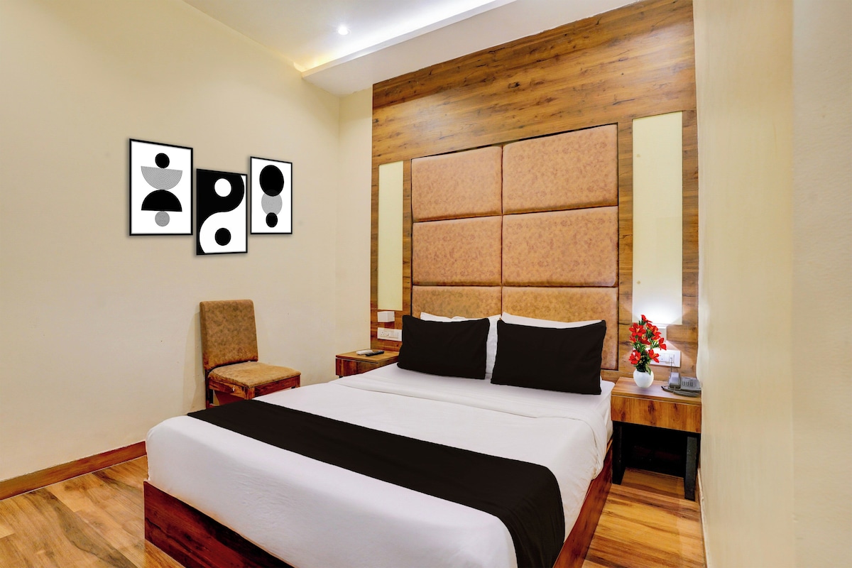 Habitación de hotel con una cama grande, cabecera de madera, una silla, mesita de noche con teléfono y una obra de arte en la pared.