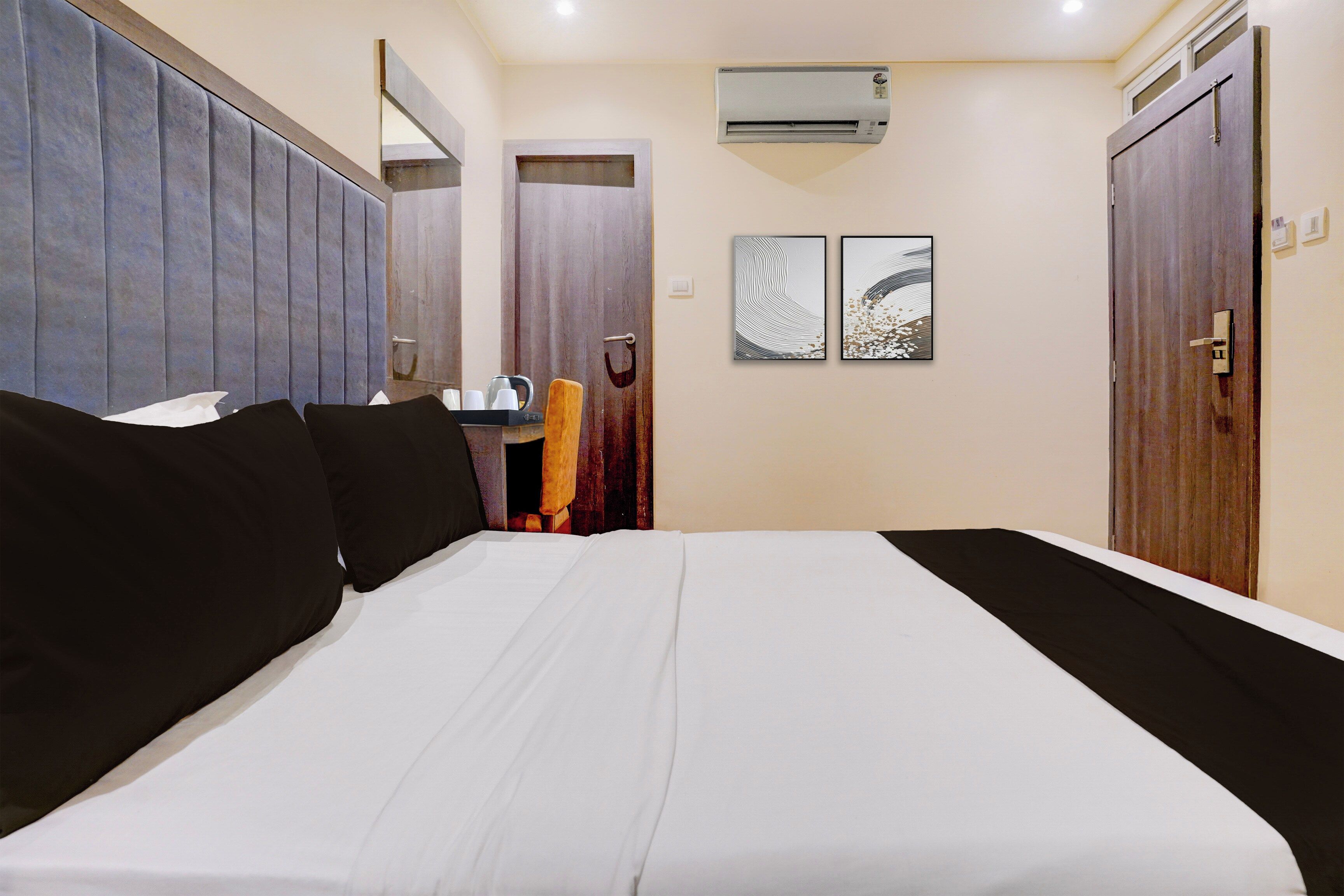 Habitación de hotel con una cama grande, un armario, un escritorio con silla y dos obras de arte colgadas en la pared.