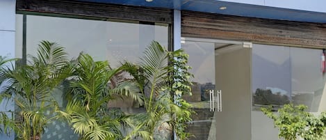 A building entrance with large glass doors, potted plants, and a fire extinguisher on the wall.