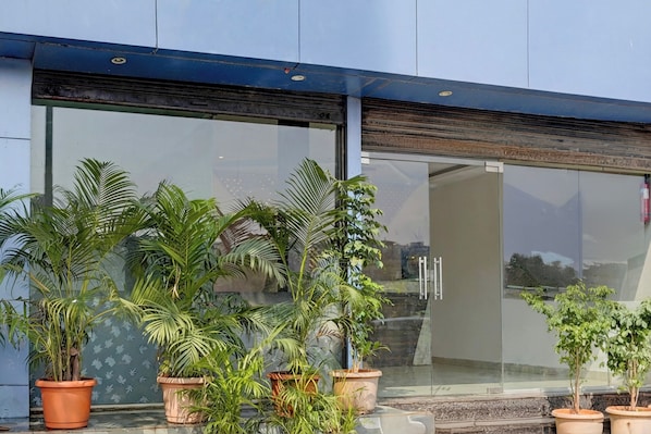 Entrada de un edificio con amplias puertas de vidrio, plantas en macetas y un extintor en la pared.