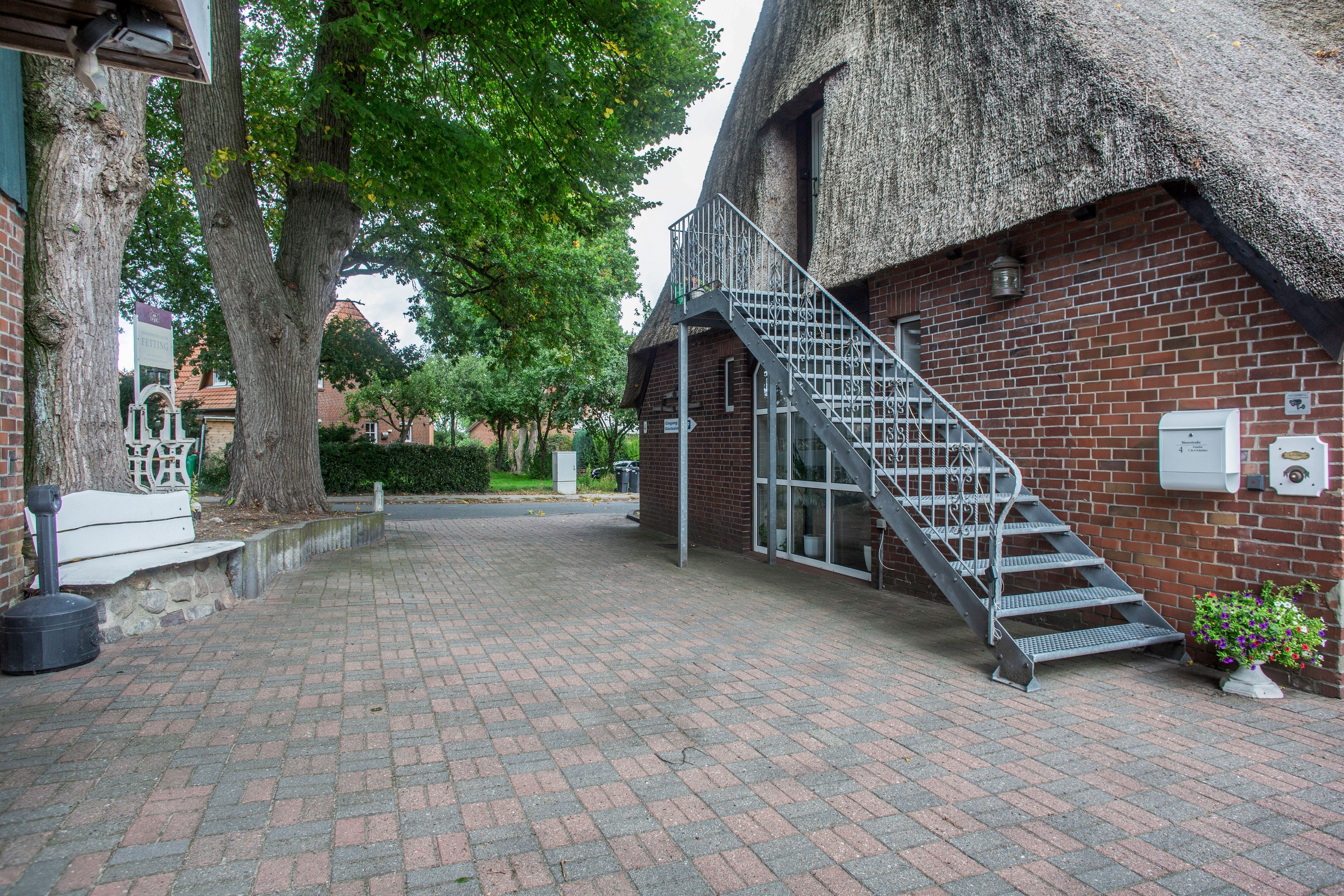 A brick building with a thatched roof, a metal staircase, and a paved walkway.